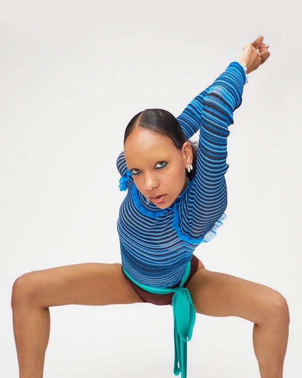 Person in a blue striped top stretching with arms raised and legs wide apart.