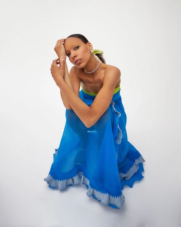 Model in a flowing blue dress poses thoughtfully against a white background.