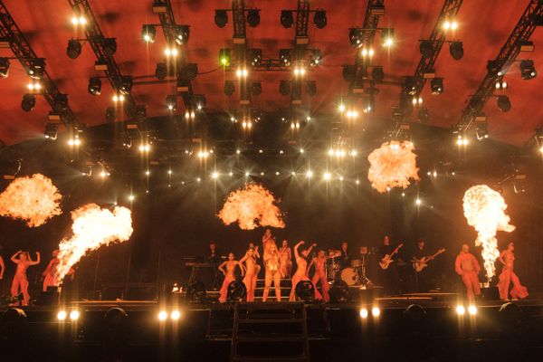 A dynamic concert stage with performers and fiery pyrotechnics.
