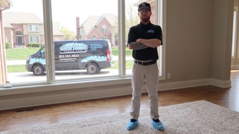 A technician stands inside a home wearing protective shoe covers and a uniform.