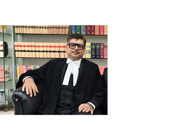 A man dressed as a lawyer sitting on a black chair in a law library.