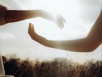Two hands reaching out towards each other in soft sunlight.