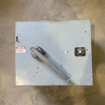 Metal electrical switch box with a large handle on a concrete floor.