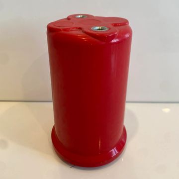 Red cylindrical object with two metal inserts on top, placed on a white surface.
