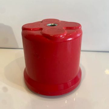 Red cylindrical object with a flower-shaped top and central screw hole.