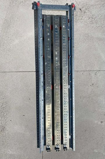 Metal scaffolding planks with holes, laid out on concrete ground.