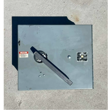 Gray electrical switch box with a large handle on concrete ground.