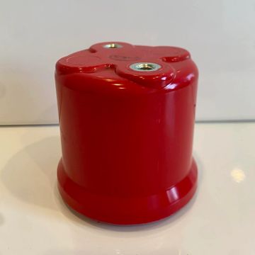Red cylindrical object with three screw holes on top.