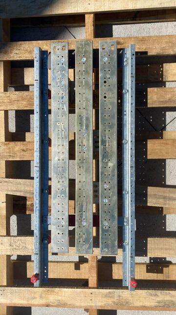 Metal beams with multiple holes laid out on a wooden pallet.