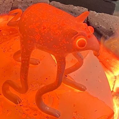 Glowing orange glass sculpture resembling a four-legged creature with distinct eyes and mouth.