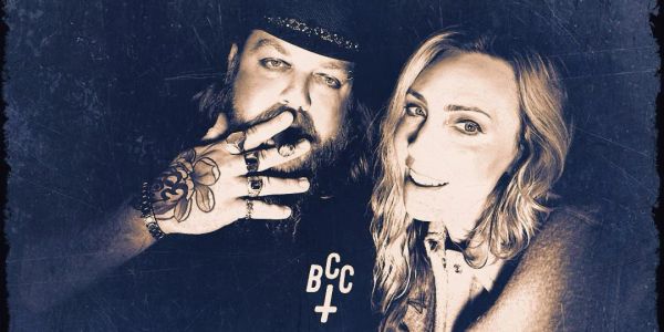 Two people posing for a close-up photo, one with tattoos and rings.
