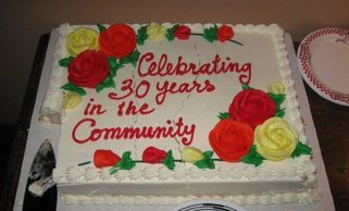 A celebration cake with red and yellow flowers honoring 30 years in the community.