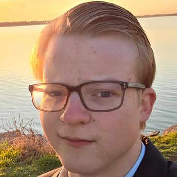 Young person with glasses near a calm lake during sunset.