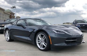 Dark gray sports car parked under cloudy sky.