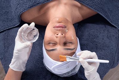 Woman lying on a grey towel having a nimue skin technology face peel.