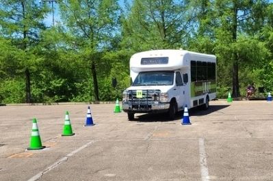 Small white bus navigating through colorful traffic cones.