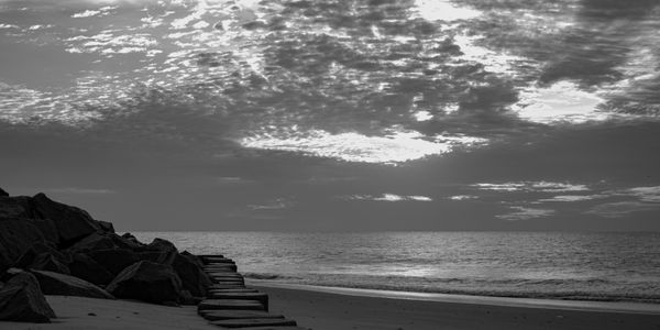 Black and white photo of a peaceful beach with dramatic clouds and calm waves.