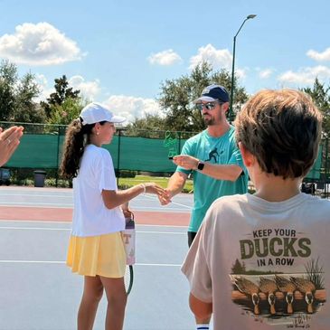 Tennis coach shaking hands with a young player on court.