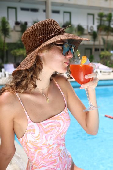Femme en maillot buvant un cocktail au bord de la piscine.