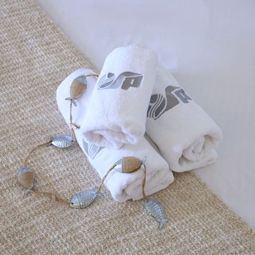 Serviettes blanches roulées sur un tapis beige avec un collier argenté.