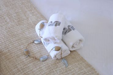 Serviettes blanches roulées sur un tapis beige avec un collier argenté.