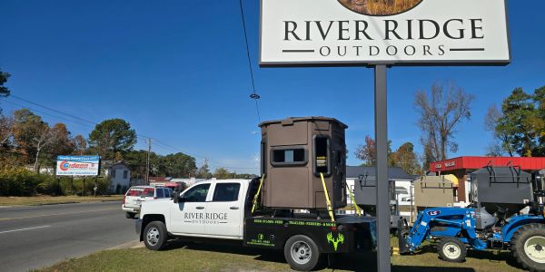 Truck with River Ridge Outdoors sign and hunting blind on the back.