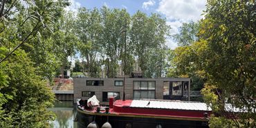 A black and red boat docked on a calm river surrounded by greenery.
