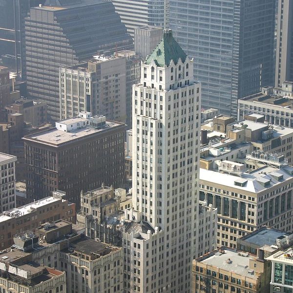 Tall historic skyscraper with a green roof amidst modern buildings.