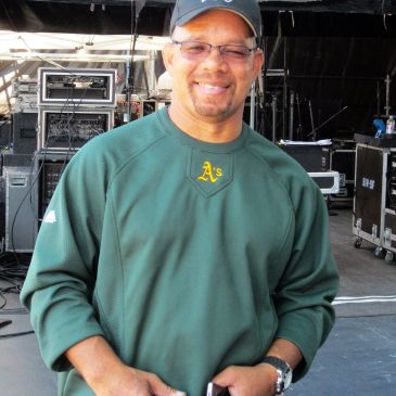 Man in green Oakland A's sweatshirt smiling.