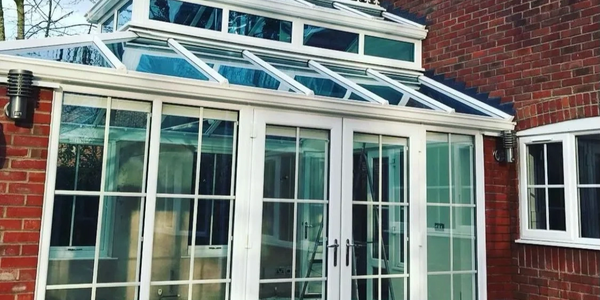 Modern glass conservatory attached to a brick house with white-framed doors and windows.