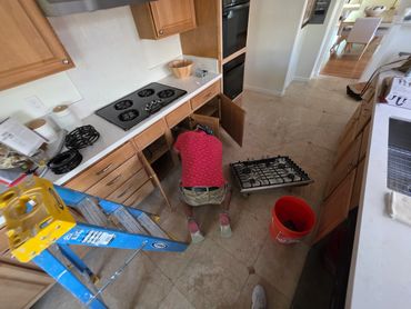 Person fixing kitchen stove with tools and open cabinets.