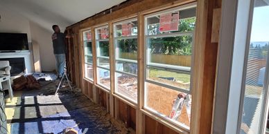 Worker installs new windows during home renovation with tools on floor.