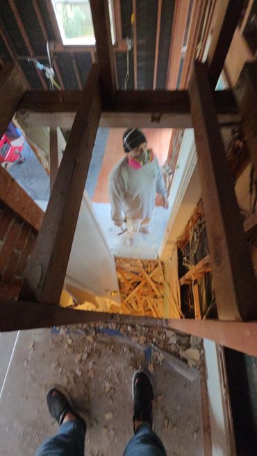 Person in protective gear in a room with exposed beams and debris.