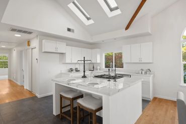 Bright modern kitchen with white cabinets, marble island, and skylights.