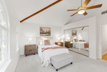 Bright bedroom with vaulted ceiling, wooden fan, and mirrored closet doors.