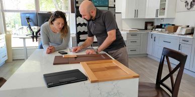 Two people discussing kitchen cabinet samples on a marble countertop.