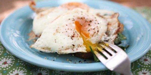 Two fried eggs with runny yolks on a blue plate with a fork.