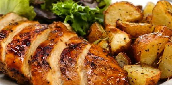 Grilled chicken breast with roasted potatoes and fresh greens on a white plate.