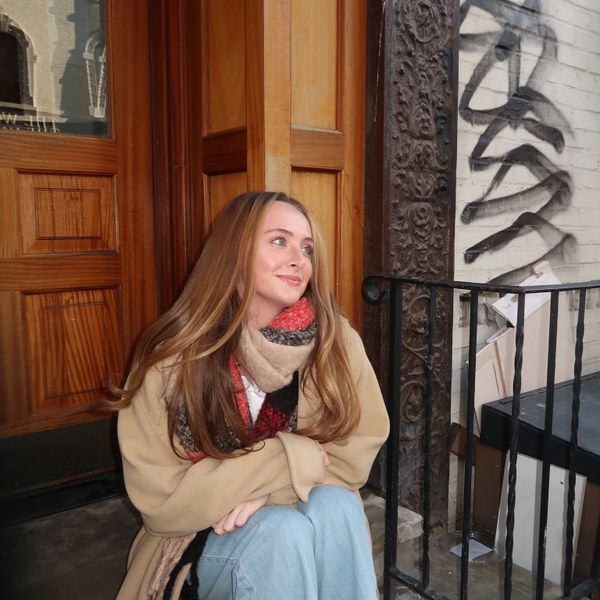 Young woman sitting outside, wrapped in a cozy scarf and coat.