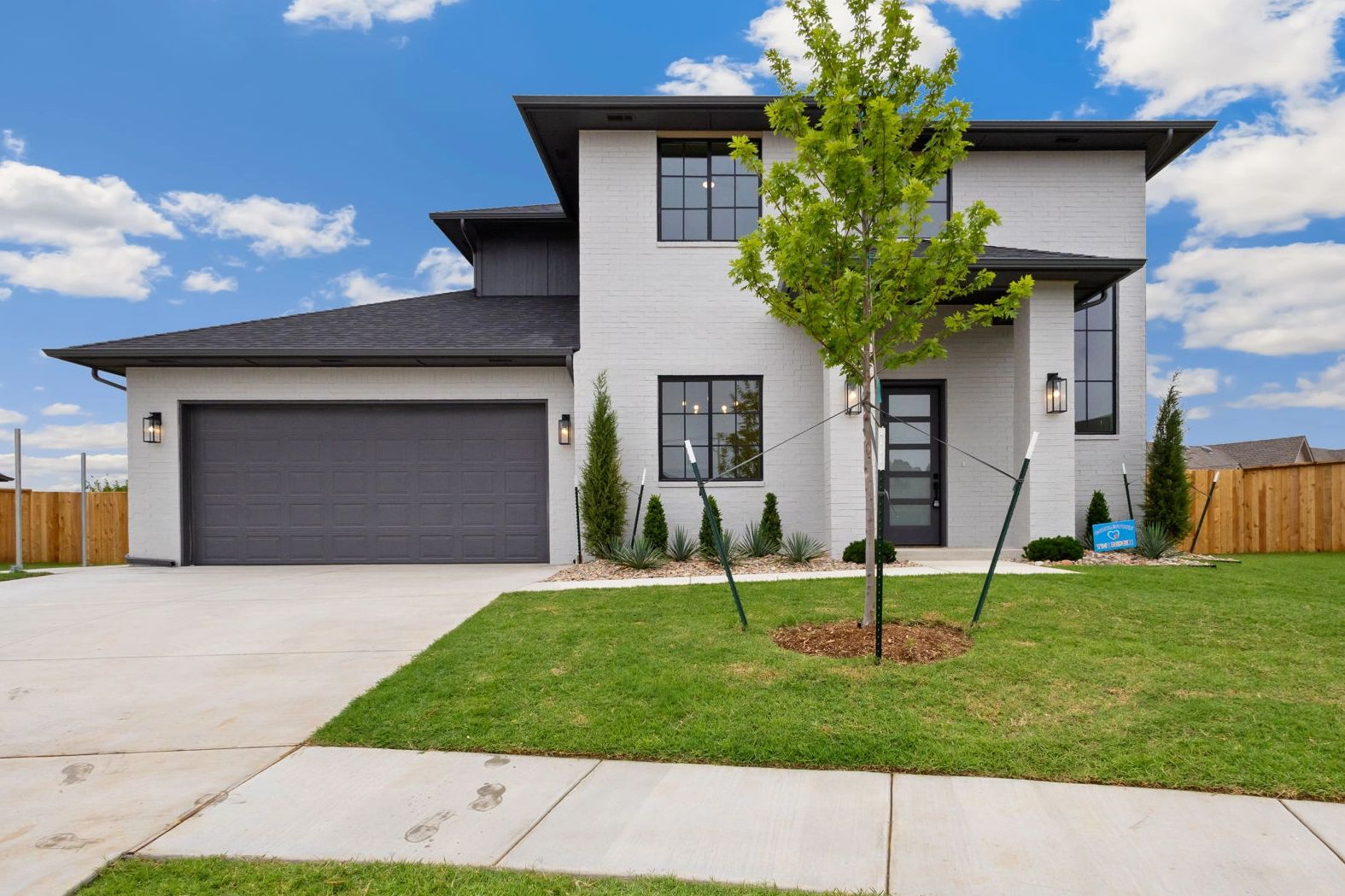 Modern two-story white brick house with black accents and a young tree in the front yard.