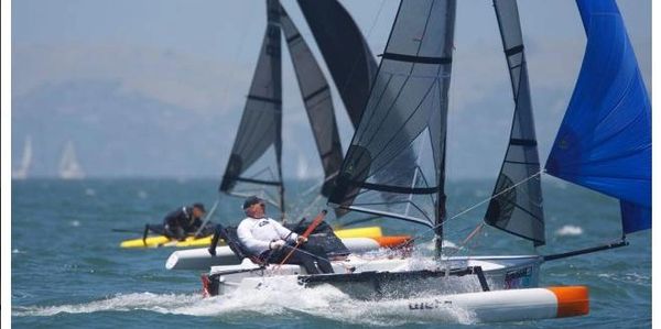 Sailboats racing on a windy day with sailors adjusting sails.