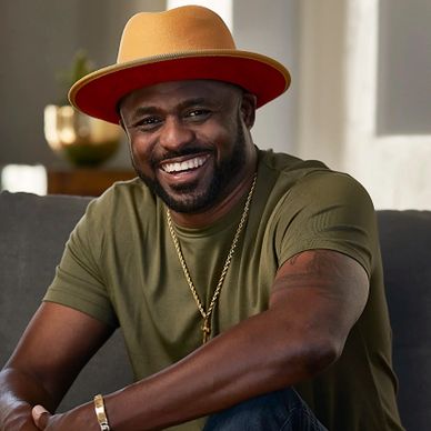 Smiling man in a mustard hat and green shirt sitting comfortably.