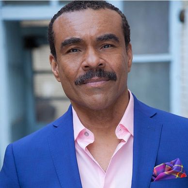 Man in blue suit and pink shirt with a mustache.