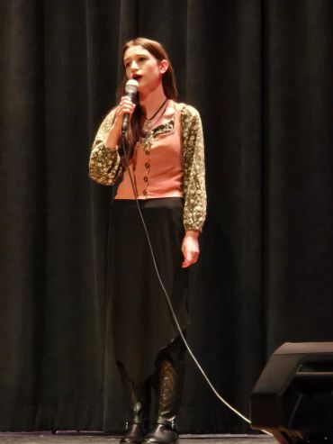 A young woman sings on stage with a microphone in hand.