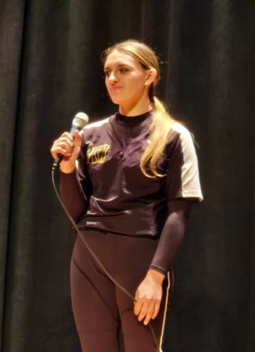 Woman in sportswear holding a microphone on stage.