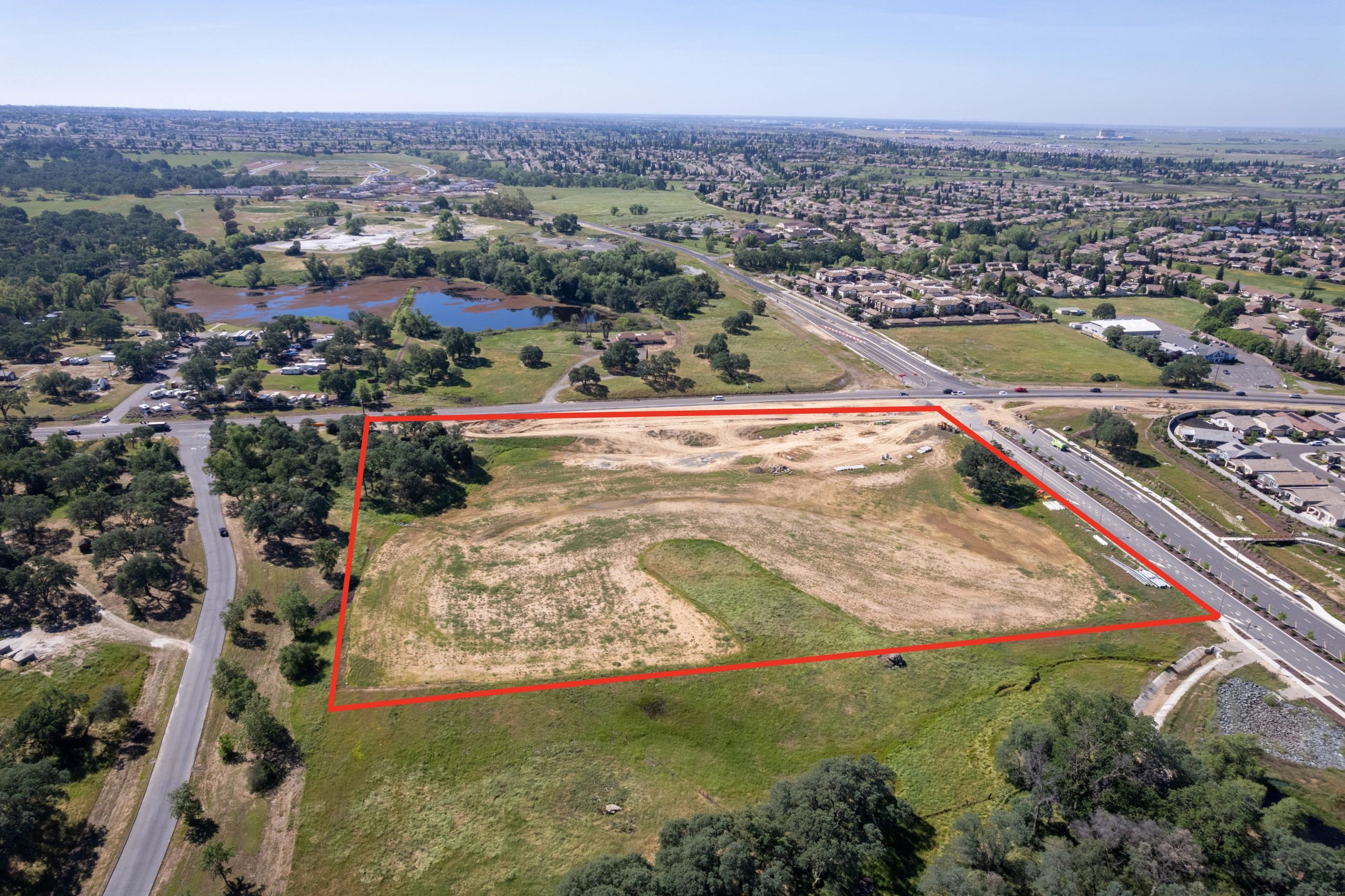 Aerial view of a large vacant land plot outlined in red near a suburban area.