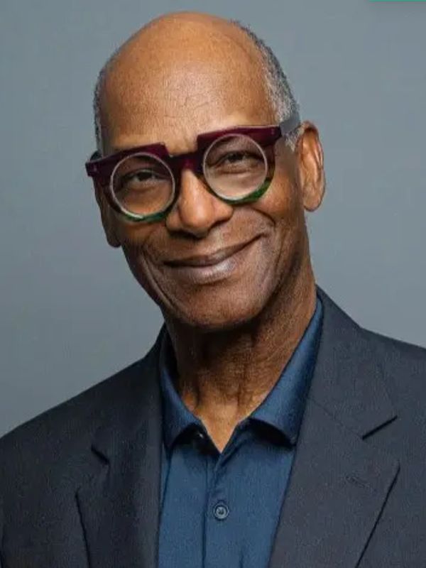 Smiling older man wearing unique round glasses and a dark blazer.