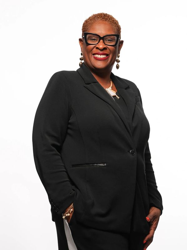Confident woman in a black suit smiling against a white background.