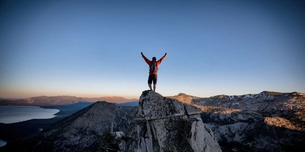 Person triumphantly stands on mountain peak at sunrise.