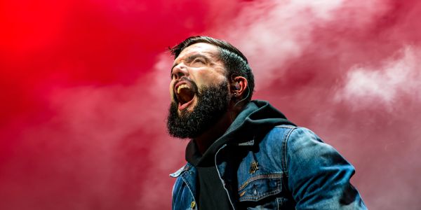 Man passionately singing on stage with red background.